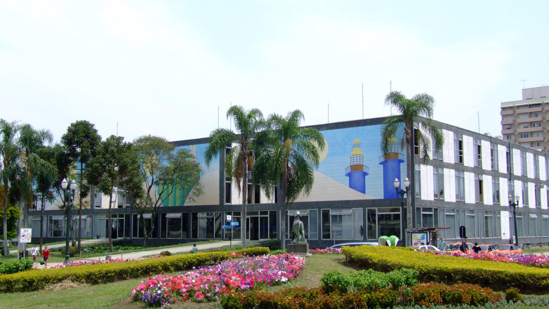 Fachada do Palácio 29 de Março, sede da Prefeitura de Curitiba, com painel de azulejos coloridos e jardim florido em primeiro plano
